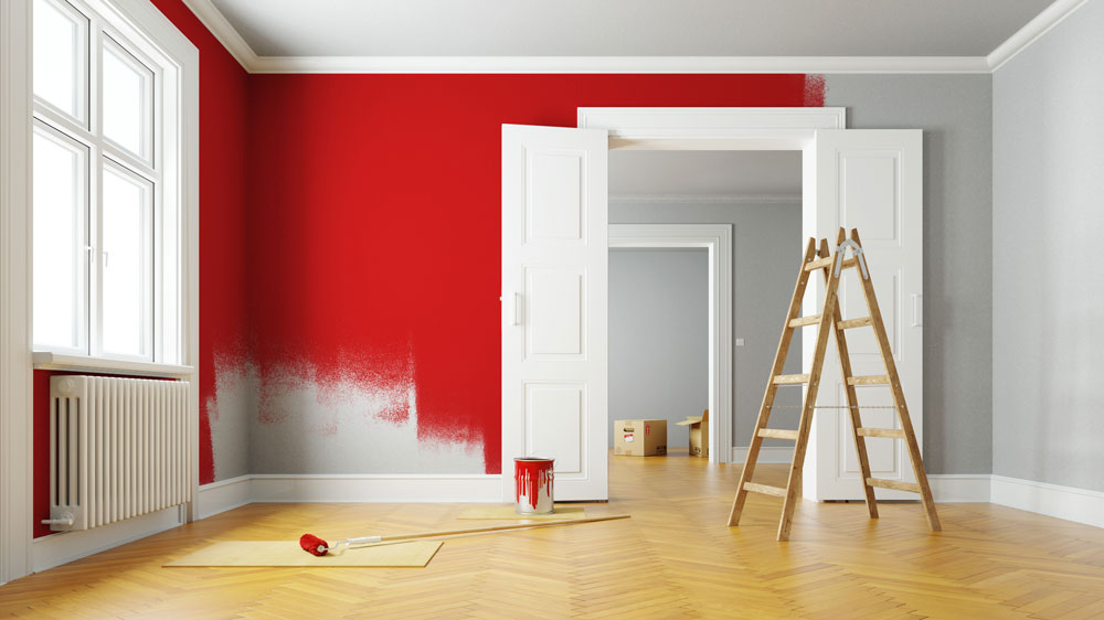 Room in a house being painted red with a ladder and wood floors with a doorway and a can of paint and a paint roller